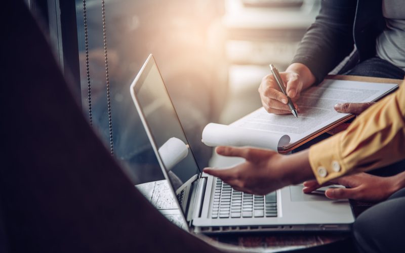 Businessmen working with laptop and smartphone in open space office. Meeting report in progress